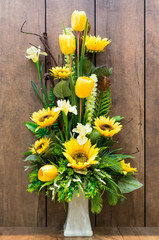 Yellow tone of artificial flower in white vase on wooden backgro