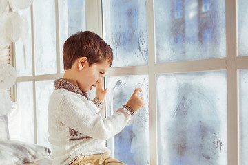 Portrait of little boy draws on a frozen window in the winter