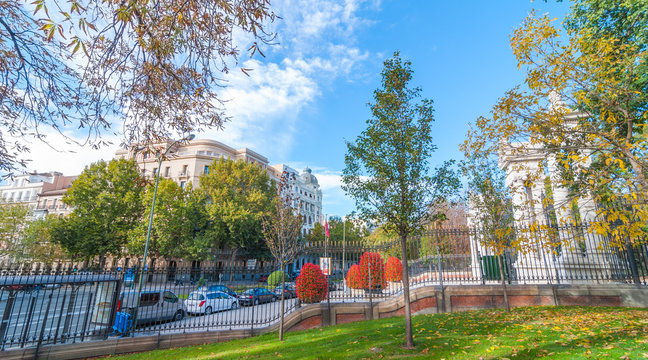 Cars parked on the side of Alfonso XII Street in Madrid, Spain, as seen from inside the fence in Retiro Park.   Unusually warm November day in one of the main parks of the city.