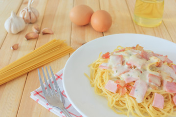 Spaghetti carbonara with chopped bacon, cheese sauce and checkered towel on white dish over wooden table background, Italian food concept.