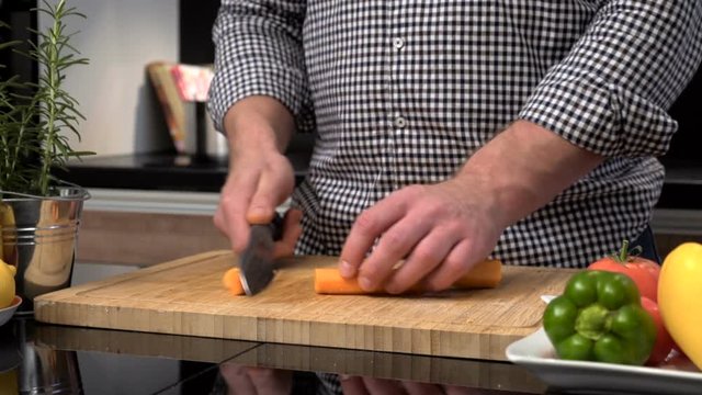 Close up on man's hands cutting carrot.
