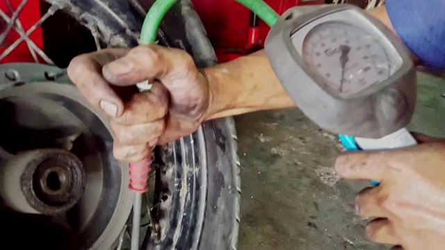 closeup macro man hands control pressure with manometer in motorcycle wheel tire in repair-shop