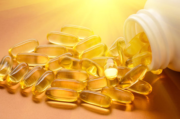 Fish oil capsules with omega 3 and vitamin D in a plastic bottle on a shiny texture with sun beams,...