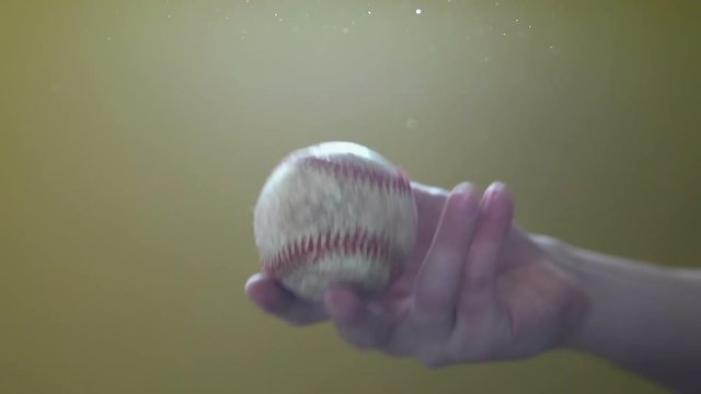 Hand tossing ball up and catching it with sunlight shining on ball.
