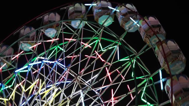 Close up of carnival lights, ferris wheel, giant rides in an amusement park at fairgrounds in Asia at night time