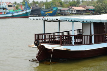 Obraz premium Thai passenger boat moored on the river with thai house style background,thai riverside folkways.
