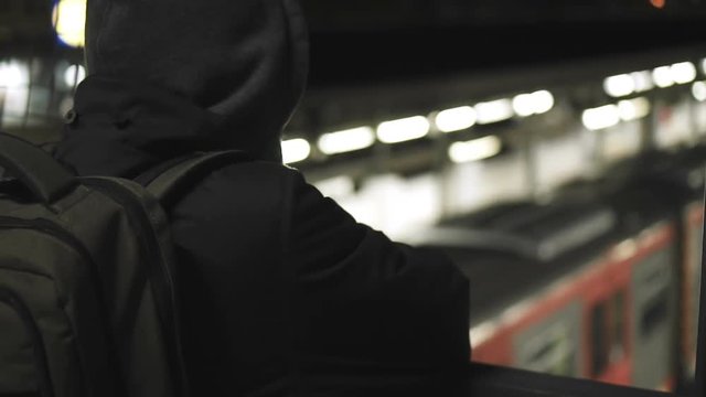 MIllenial youth in hoodie at the train station at night, slomo 100p.A hooded young man is waiting for the train or walking along the platform with or witout his hoodie on, at night.