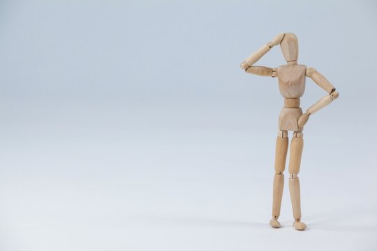 Confused wooden figurine standing with hand on head