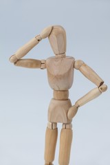 Confused wooden figurine standing with hand on head