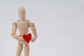 Wooden figurine standing and holding a red heart in front