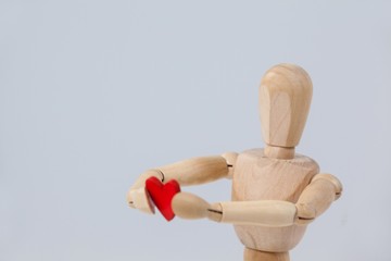 Wooden figurine holding a red heart in front