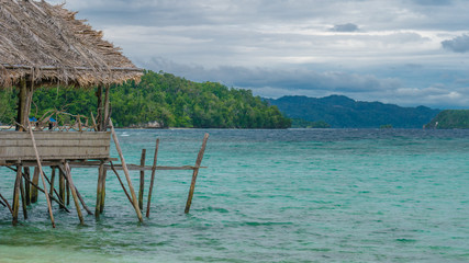 Beautiful Blue Lagoone with some Bamboo Huts, Kordiris Homestay, Palmtree in Front, Gam Island, West Papuan, Raja Ampat, Indonesia