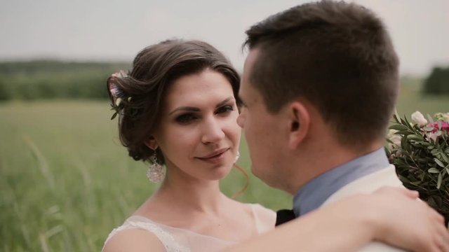 Close-up of a beautiful bride. She hugs her groom and tenderly looks in camera then into his eyes. Wedding day
