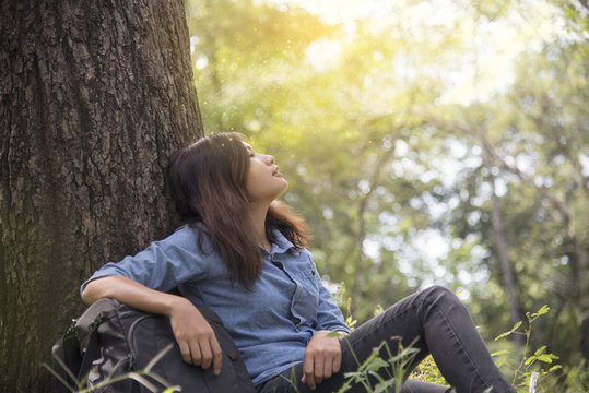 Happy woman enjoy and relax with the nature. Young beautiful woman sitting under the big tree in green forest.