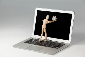 Wooden figurine cleaning the screen of laptop 