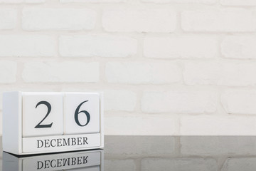 Closeup white wooden calendar with black 26 december word on black glass table and white brick wall textured background with copy space , selective focus at the calendar