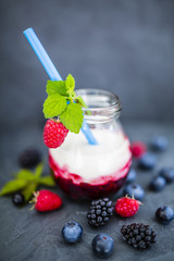 Yogurt with fresh berries fruit on dark stone background.