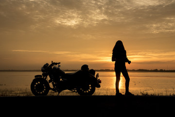 Obraz na płótnie Canvas Beautiful Woman biker enjoying sunset, female riding motorcycle. motorbike driver traveling the world, Relaxing after long trip, freedom lifestyle. Travel Concepts.