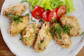 fried chicken wings or fried chicken with vegetable and sauce on white dish. fried chicken is bad cholesterol and bad for health when eating a lot. fast food for who work in city or office.