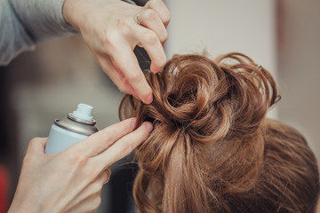 Closeup of hairdresser hands using hairspray styling on woman's healthy golden hair at barber salon