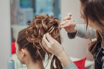 Hairstylist makes the bride with blond hair beautiful high hairdress at the salon