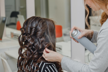 Stylist curling hair and making wedding hairstyle for brown haired woman.