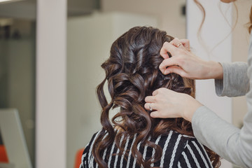 Naklejka premium Close up of hands of professional hairdresser at beauty salon, curling female hair