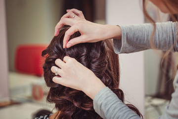 Fototapeta premium Stylist curling hair and making wedding hairstyle for brown haired woman.