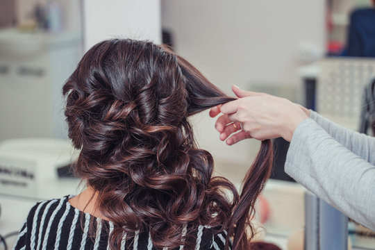 Stylist curling hair and making wedding hairstyle for brown haired woman.