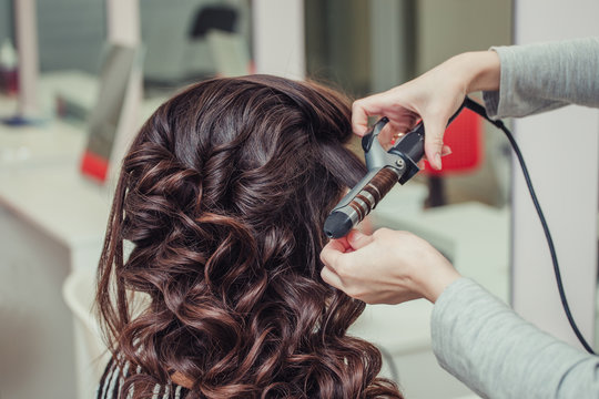 Hairdresser doing wrap curling brunette hair in a beauty salon with iron