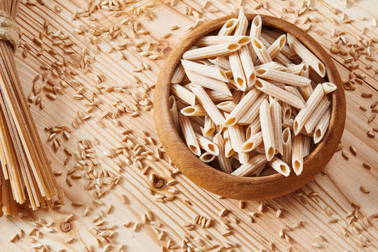 Uncooked Whole Wheat Pasta In Wooden Bowl Surrounded By Wheat