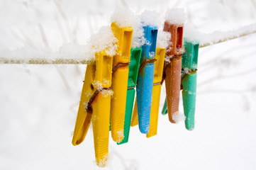 Colorful clips for washing laundry covered with snow on strip rope outdoor.
