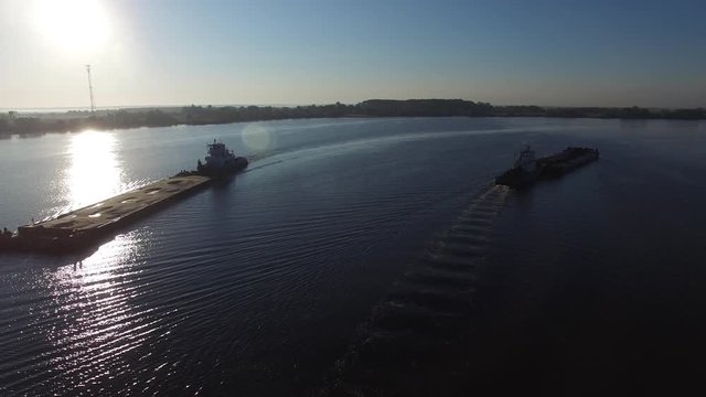 Cargo transport ships sailing on a wide river. Summer dawn. Two barge floating in the river at dawn. Aerial view.