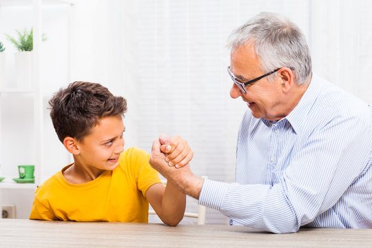 Grandfather and grandson arm wrestle at home. 