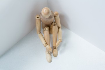 Wooden figurine sitting against wall - Powered by Adobe