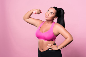Obraz premium Pretty plump woman posing with small dumbbell