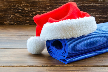 Close up of blue mat with Santa Clause hat on wooden background. Best Christmas gift for active person. Yoga xmas concept.  Copy space. © vasanty