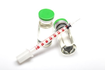 Transparent medical insulin syringe lying on medical bottle with hormone. Another insulin ampule with green cap standing near. White background, shadows. close up image.