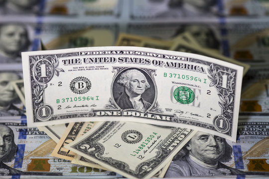 One us dollar bill standing on hip of us banknotes. Hundred us dollar banknotes background. close up image. Selective focus and light.
