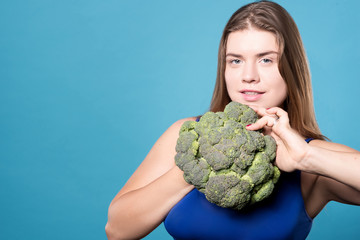 Pleasant plump woman standing with broccoli