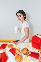 Woman with white mug sitting and refusing from fast food