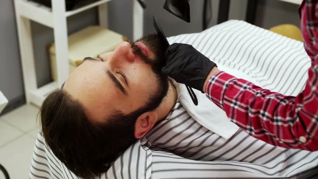 Barber woman trimming beard of client with clipper at barbershop.
