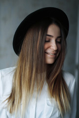 portrait of a girl brunette in black hat and white shirt. She is smiling cute and looking down