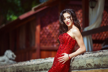 Young woman with long hair posing in red stone dress in luxury place