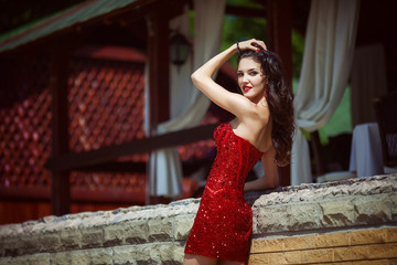 Beautiful young woman with long hair posing in red dress in luxury place