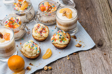 Homemade desserts - biscuits with yogurt, tangerines and walnuts in glass, oats with fresh fruit in glass jar and cupcakes with white frosting and sprinkles.