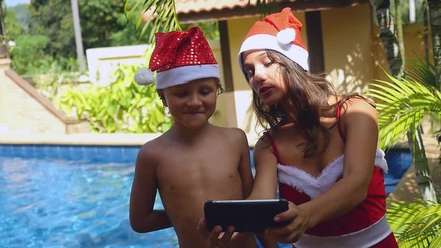 Playful smiling mother and child wear christmas hats taking picture self portrait on smartphone together in slow motion near the swimming pool on tropical island of Koh Samui. Thailand. 1920x1080