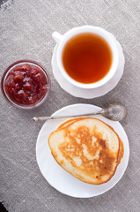 Top view of plate of hot pancakes, cup of tea and strawberry jam