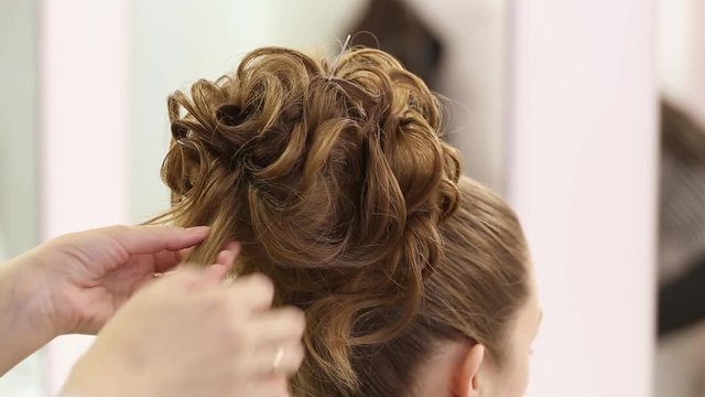 Professional hairdresser doing hairstyle with bun and curls for beautiful healthy hair