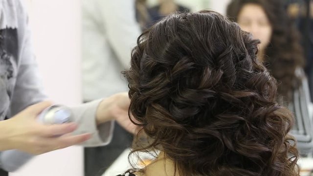 Close-up of hairdresser's hands using hairspray on brunette hair at beauty salon.